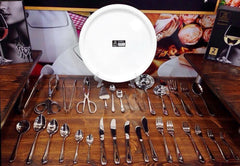 Set of silverware including forks, knives, and spoons on a wooden surface with a white plate in the center.