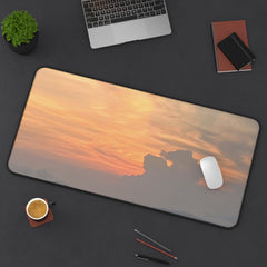 Desk setup with a large mouse pad featuring a sunset design, laptop, cup, and office supplies.