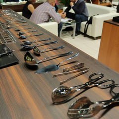 Row of silver spoons on a wooden surface with people in the background