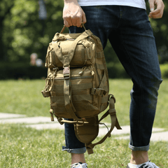 Person holding a tactical backpack outdoors on a grassy area