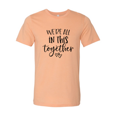 Peach t-shirt with black text 'We're all in this together' on a white background