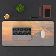 Desk setup with a laptop, mouse, and stationery on a large desk mat featuring a sunset design.