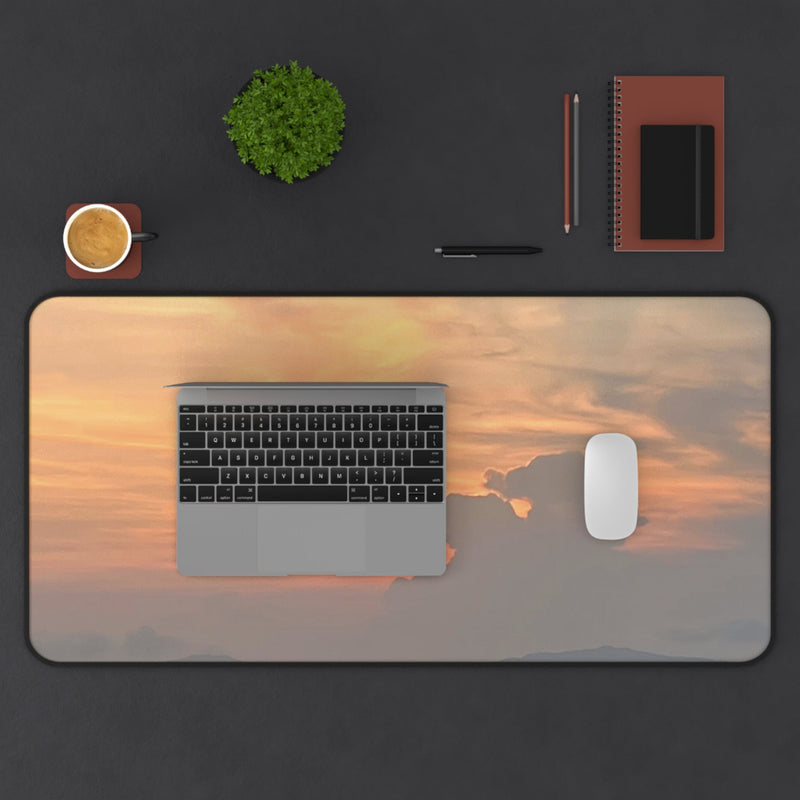 Desk setup with a laptop, mouse, and stationery on a large desk mat featuring a sunset design.