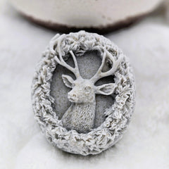 Decorative stone with deer head and floral wreath on a marble surface