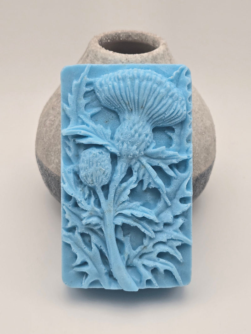 Blue soap bar with thistle design on a stone vase and light surface