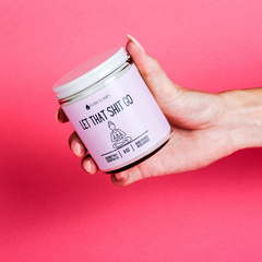 Hand holding a jar labeled 'Let That Shit Go' against a pink background