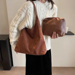 Person holding a brown leather bag and clutch against a neutral background
