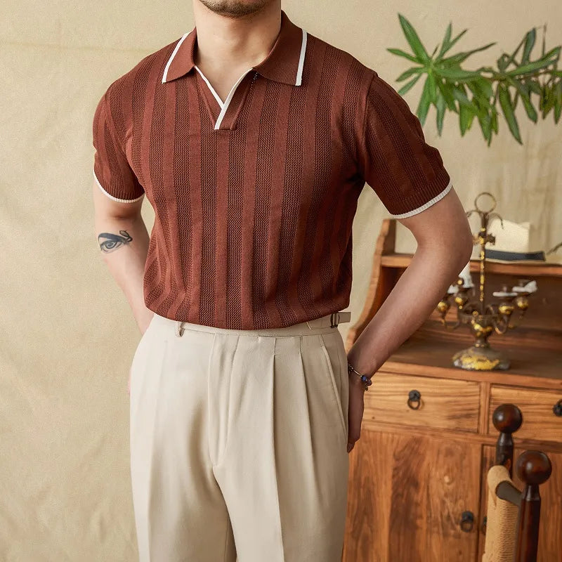 Man wearing a brown striped shirt and beige pants standing in a room with wooden furniture and plants.