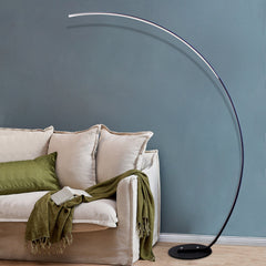 Modern floor lamp with a curved design next to a beige sofa with green cushions and blanket against a blue wall.