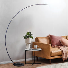 Modern living room with a brown leather sofa, round floor lamp, and small table with a plant and mug.