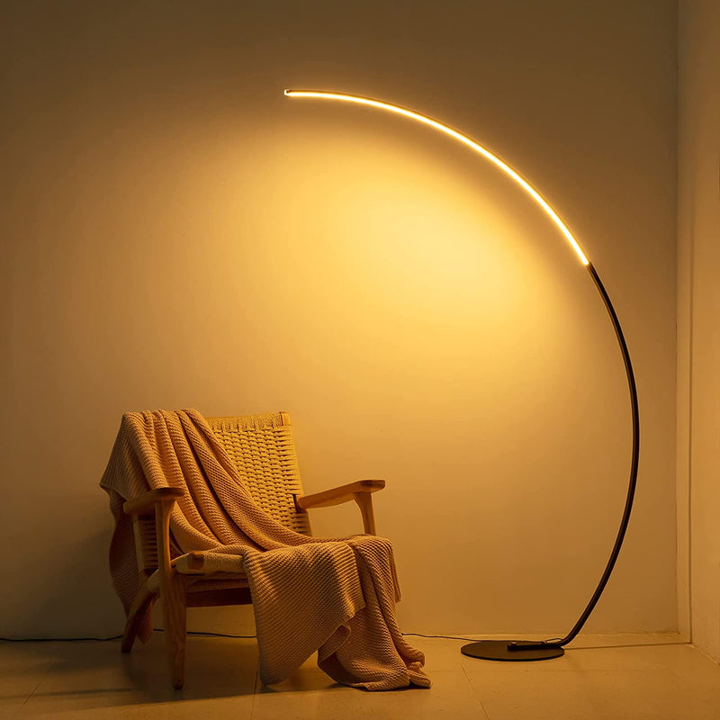 Curved floor lamp casting a warm glow over a chair with a blanket in a softly lit room.