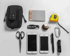 Collection of everyday carry items including a black pouch, scissors, phones, and tools on a light gray background.