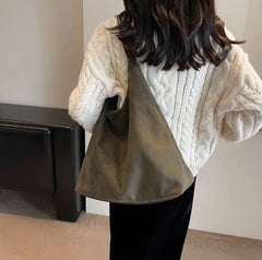 Person wearing a white cable knit sweater holding a dark green bag indoors.