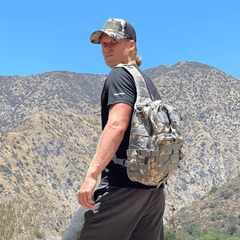 Man with a camouflage backpack standing in a mountainous area