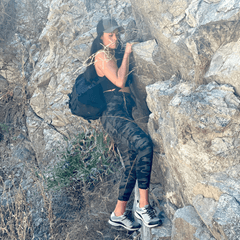 Person climbing a rocky incline wearing a black outfit and cap.