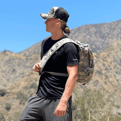 Man with a backpack and camouflage cap standing in a mountainous area
