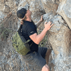 Person climbing a rocky mountain with a green backpack