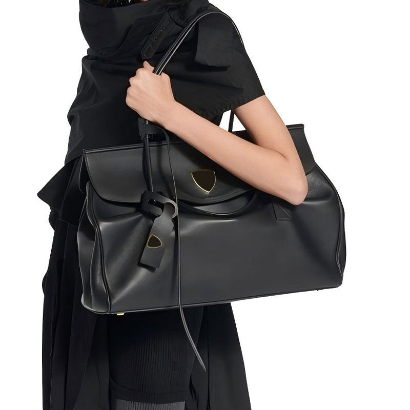 Person holding a black leather handbag with gold accents on a white background