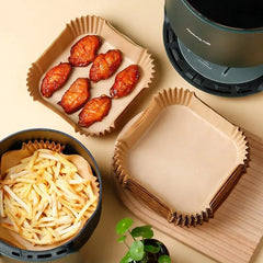 Air fryer basket with cooked food and paper trays on a beige surface.
