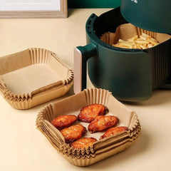 Green air fryer with paper baskets containing food on a beige surface