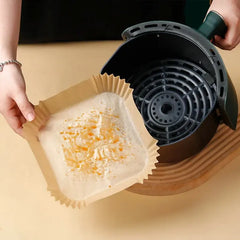 Person holding a brown paper insert with residue on a beige surface and an air fryer basket