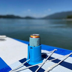 Can in a blue holder on a paddleboard with a lake and mountains in the background