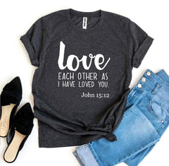 Dark gray t-shirt with 'love each other as I have loved you' text, paired with jeans and shoes on a white background