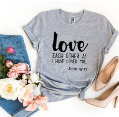 Gray t-shirt with 'love each other as I have loved you' text, jeans, flowers, and high heels on a white background