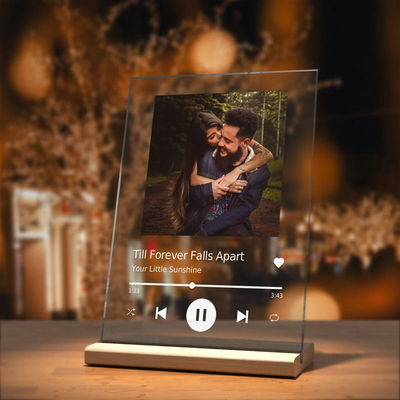 Clear digital photo frame displaying a couple in a forest with a music interface on a wooden surface.
