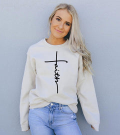 Woman wearing a sand colored sweatshirt with 'faith' printed on it against a gray background