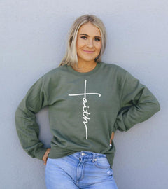Woman wearing a green sweatshirt with 'faith' and a cross design against a light gray background