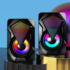 Pair of black speakers with colorful LED lighting on a reflective surface with a blue gradient background.