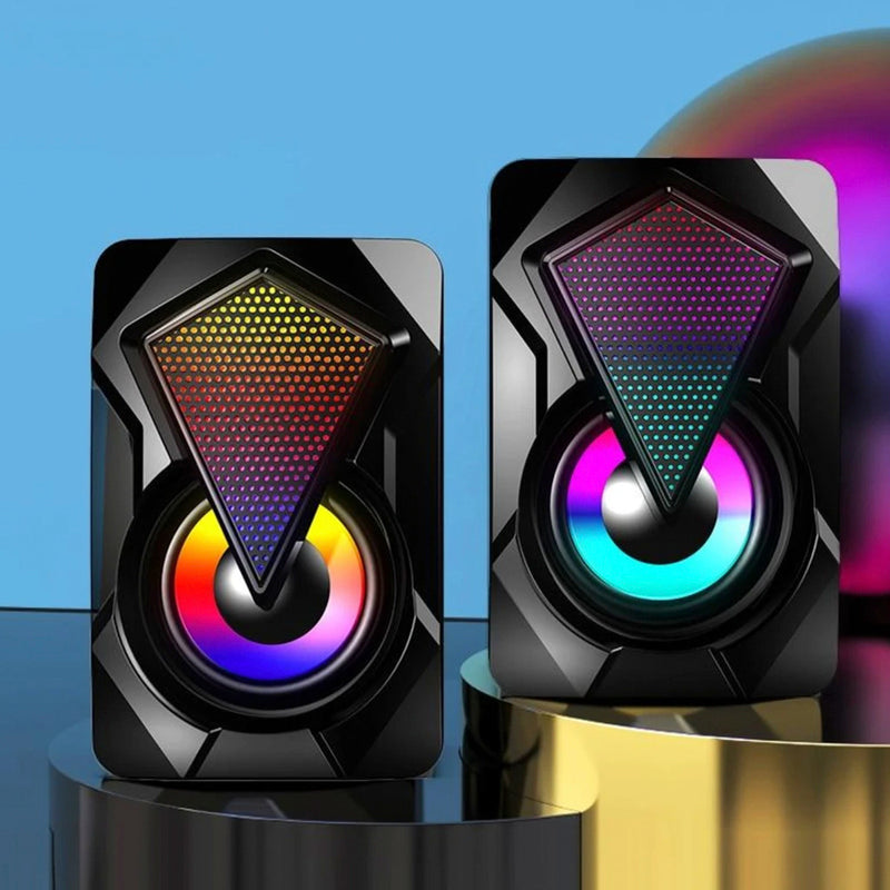Pair of black speakers with colorful LED lighting on a reflective surface with a blue gradient background.