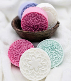 Decorative soaps with intricate patterns in a wooden bowl on a soft white background