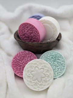 Decorative soaps with intricate designs in a wooden bowl on a soft fabric background