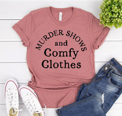 Mauve t-shirt with 'MURDER SHOWS and Comfy Clothes' text, paired with jeans and sneakers on a white wooden surface.