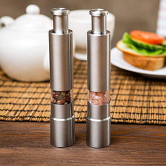 Two metallic salt and pepper shakers on a wooden table with a blurred background of a teapot and sandwich.