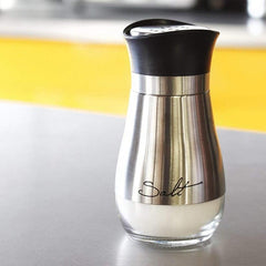 Silver salt shaker with black lid on a kitchen counter