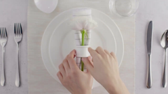 Person arranging a flower on a white plate with cutlery around